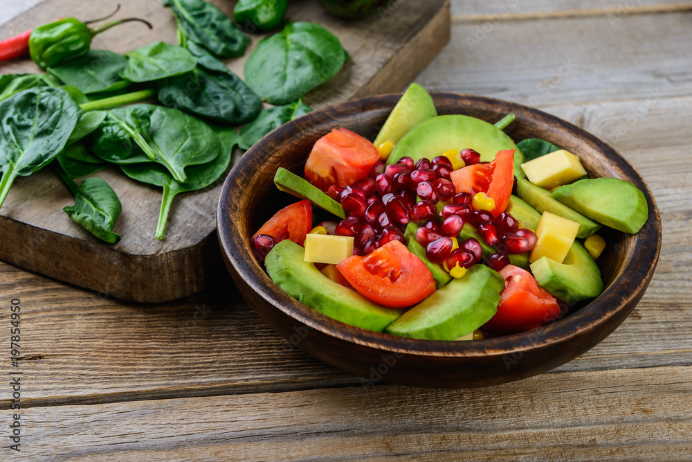 Healthy salad with avocado, tomatoes, pomegranate and baby spinach  in a bowl on a rustic wooden background