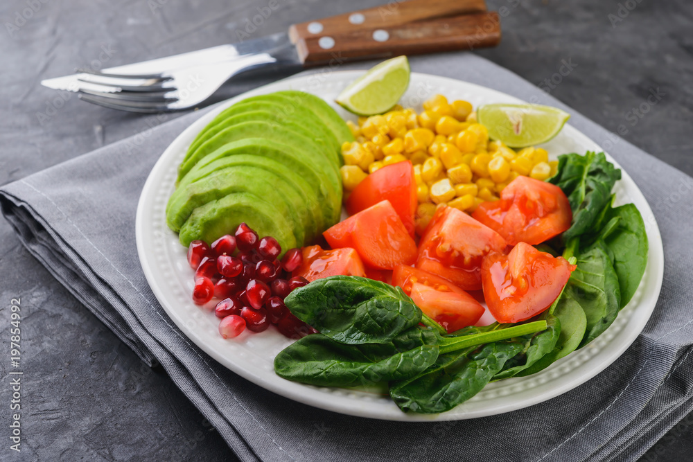 Fresh avocado salad with tomatoes, pomegranate, spinach, lime and corn on dark background Healthy food concept. Fresh avocado salad with tomatoes, pomegranate, spinach, lime and corn on dark background Healthy food concept.
