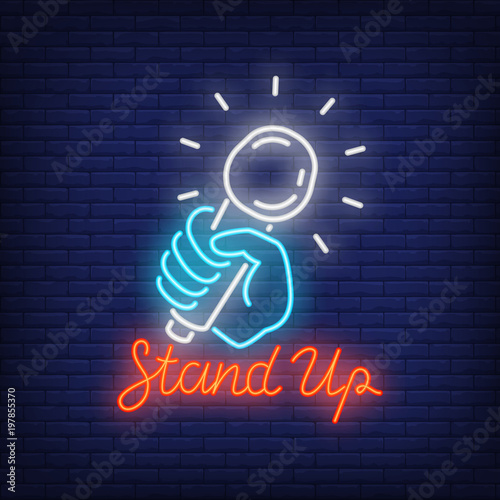 Stand up neon sign. Microphone in human hand on brick wall background. Night bright advertisement. Vector illustration in neon style for comedy show