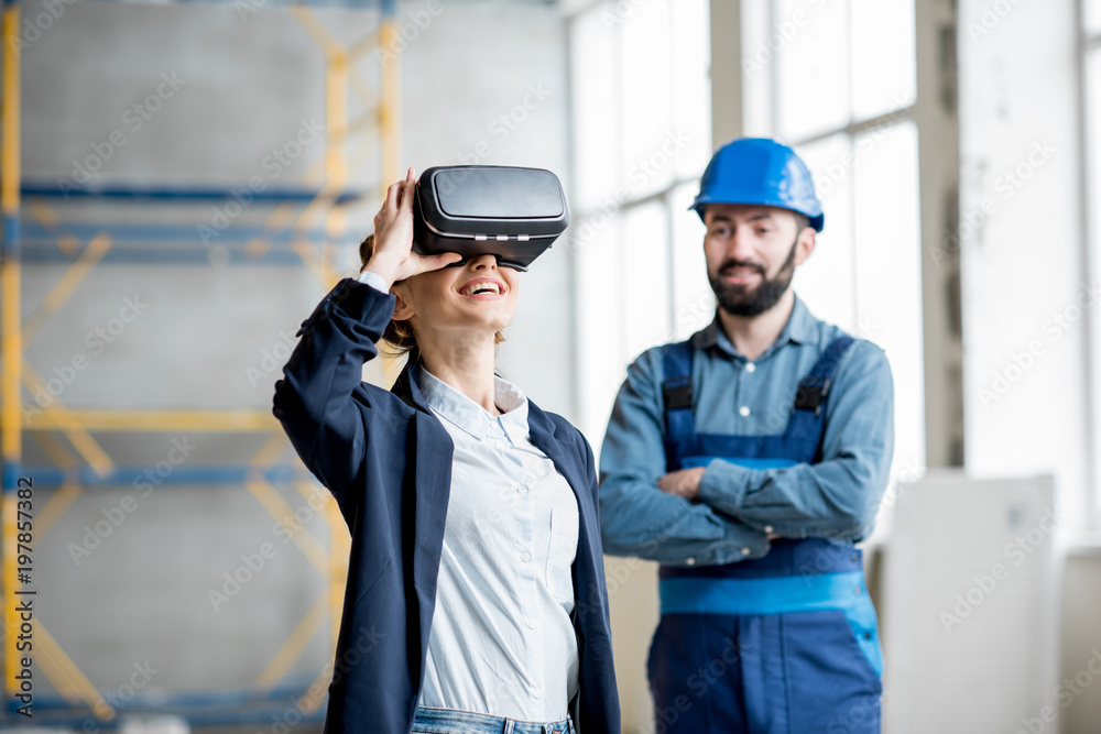 Woman client wearing VR glasses imagining future interior standing with builder at the construction site Woman client wearing VR glasses imagining future interior standing with builder at the construction site