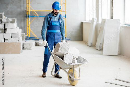 Photo Builder carrying blocks on a wheelbarrow at the construction site indoors