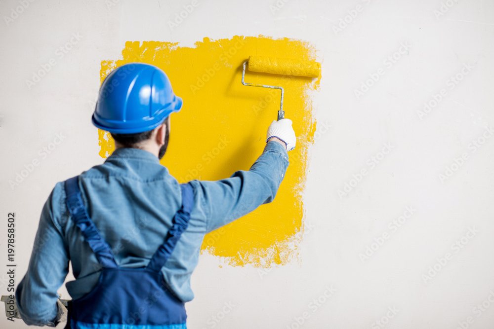 Φωτογραφία Workman in uniform painting wall with yellow paint at the construction site indo