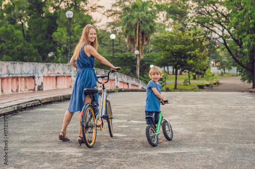 Happy family is riding bikes outdoors and smiling. Mom on a bike and son on a balancebike photo