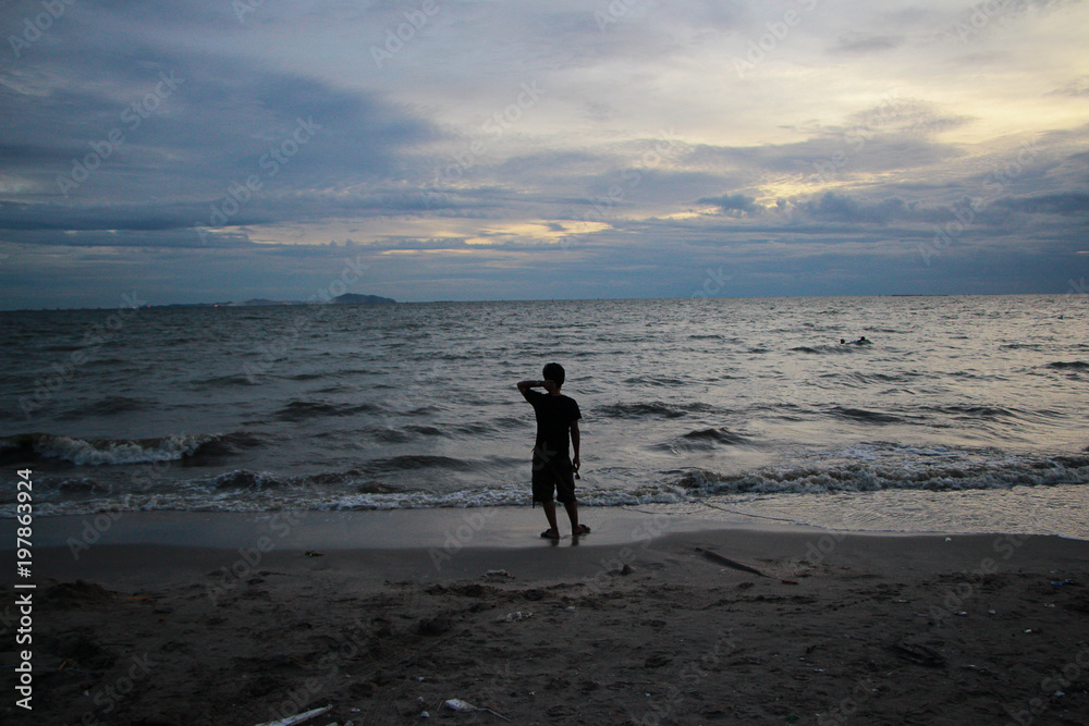 Naklejka premium a man looking for and walking on the beach at sunset