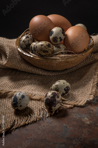 Chicken and quail eggs in bowl on rustic wooden background