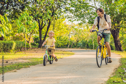 Happy family is riding bikes outdoors and smiling. Father on a bike and son on a balancebike photo