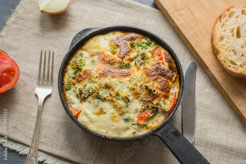 Traditional French omelette with broccoli and tomatoes in a frying pan on a rustic background