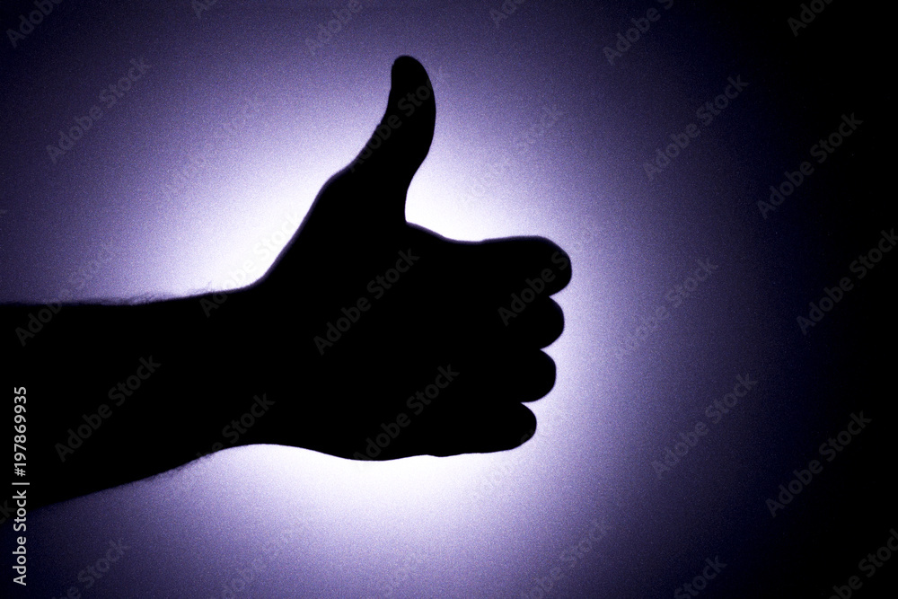 Thumbs up. Silhouette of a man's hand against a background of a bright blue light circle like the moon.