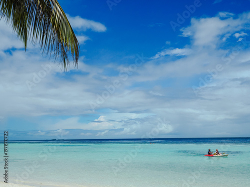 Idyllic white beach with palm trees and people kayaking © Luoxi
