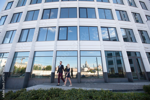 Man and woman walk hand against the glass of the building.