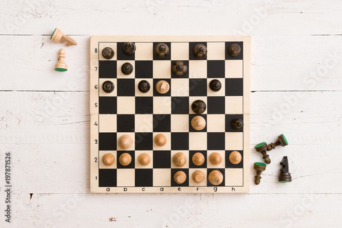 Top view on wooden chess board with figures during the game on white wooden tabl Fototapeta