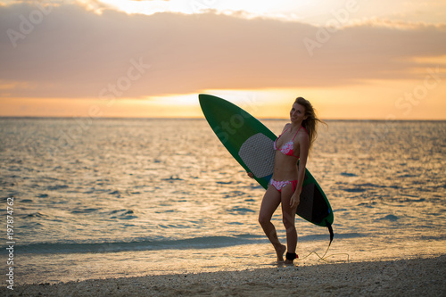 Surfing surfer girl looking at ocean beach sunset. Silhouette of female bikini woman looking at water with standing with surfboard having fun living healthy active lifestyle. Water sports with model..