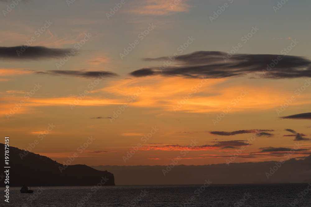 Boat sailing on the Atlantic Ocean at dawn under the beautiful colorful sky with interesting clouds just before sunrise