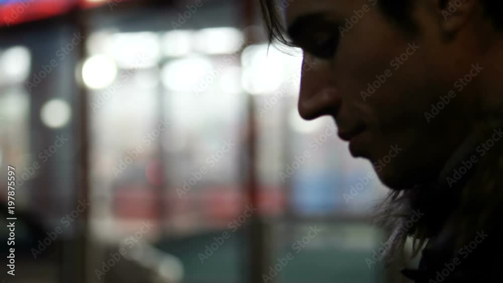 Handsome trendy man recording voice message on cell phone that he is holding, outdoor at night in city setting