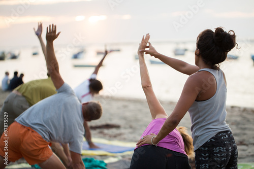 Women doing yoga exercises or supported pigeon pose on an empty beach of the Indian ocean in Mauritius