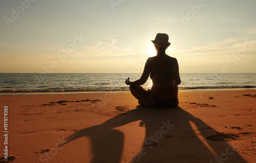 A female person meditating on the sand beach at sunset