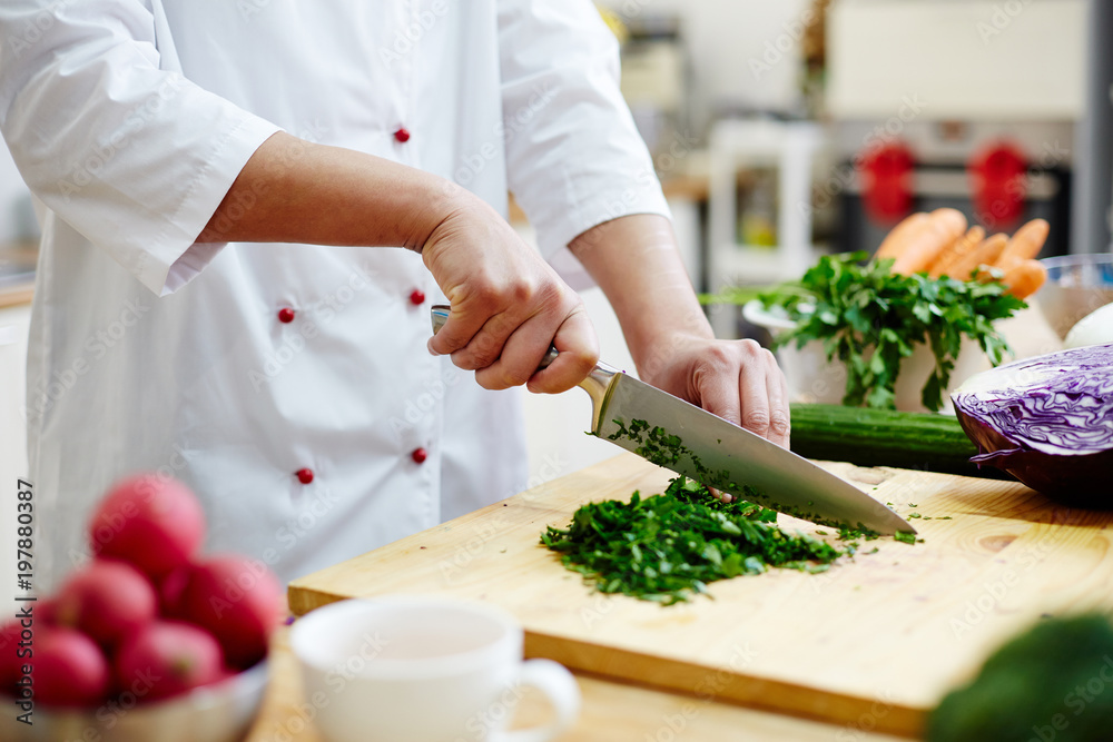 Chef cutting greenery with sharp professional knife on wooden board while cooking in the kitchen Chef cutting greenery with sharp professional knife on wooden board while cooking in the kitchen