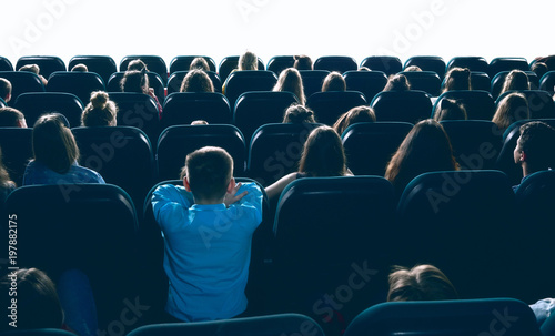 great ammount of people watching movie in big cinema hall, sitting on comfortable places. Backview of women, men and children entertaining in cinema house.