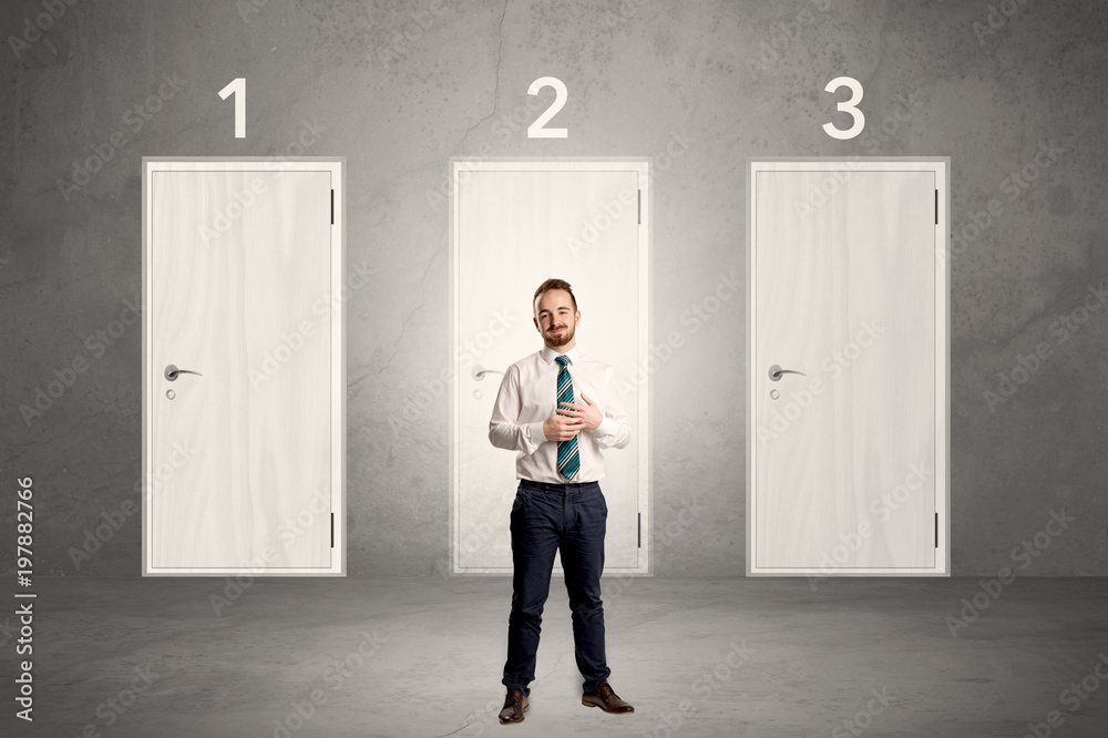 Fototapeta premium Businessman in grey room with three numbered white door behind his back 