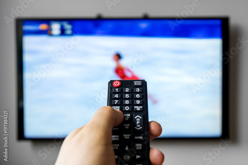 Male hand holding TV remote control. Figure skating.