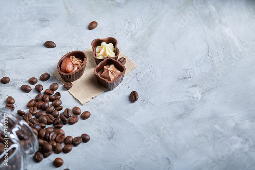 Side view of overturned glass jar with coffee beans and chocolate candies on wooden background, selective focus photo