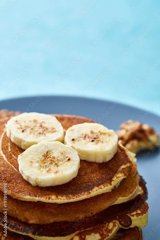 Pile of homemade pancakes with walnuts on blueish plate over blue background, selective focus