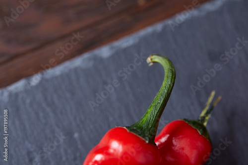 Composition of tomato bunch and hot pepper on black piece of board, top view, close-up.
