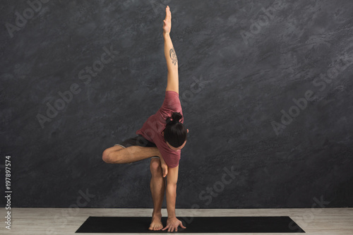 Young flexible man practicing yoga at gym
