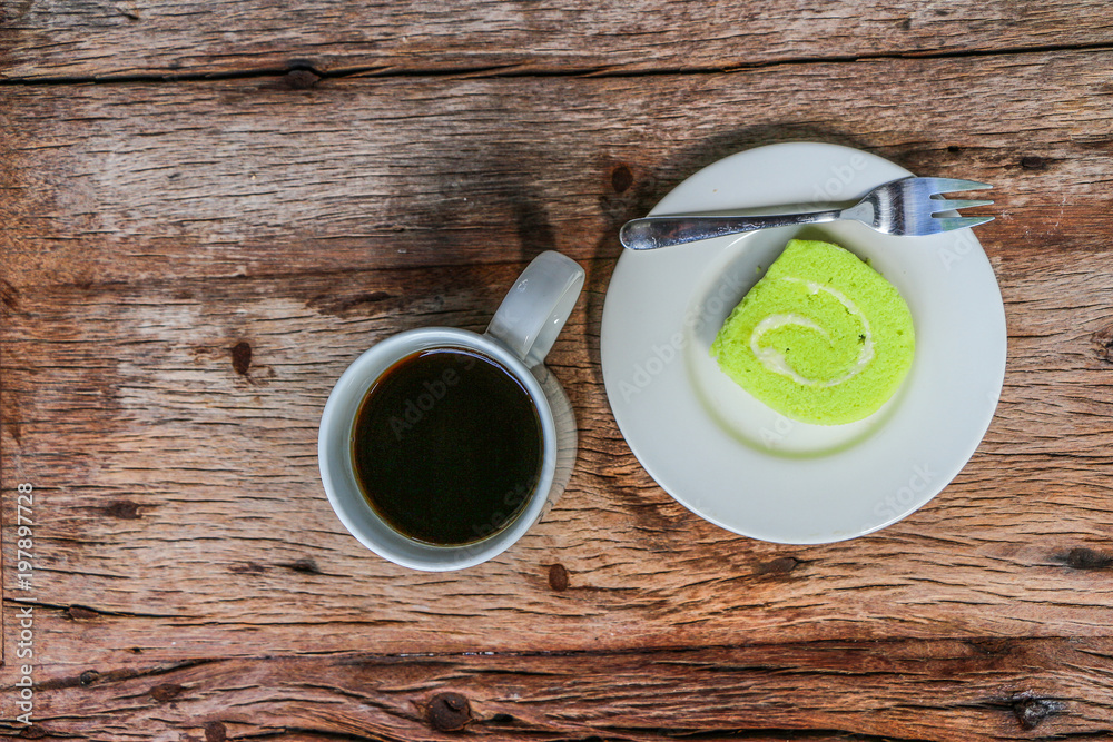 Green Jam Roll Cake with back coffee on Wooden Table	