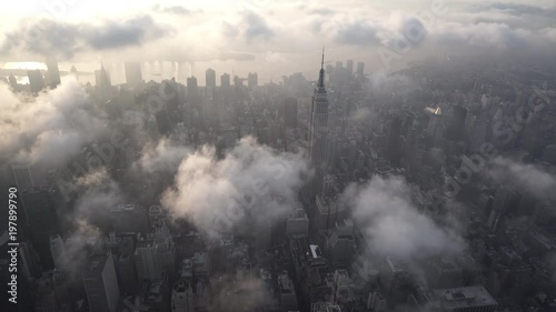 New York City aerial view approaching the Empire State Building at sunrise, with Midtown Manhattan skyscrapers under low level clouds and fog.
