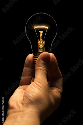 Hand holding a filament lamp on a black background. The bulb as a symbol of an idea. Glowing tungsten bulb. Ecological concept.