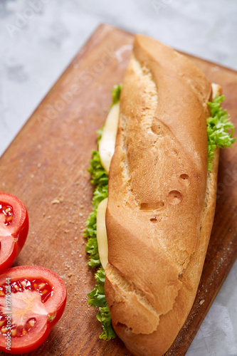 Fresh and tasty sandwich with cheese and vegetables on cutting board over white textured background, selective focus.