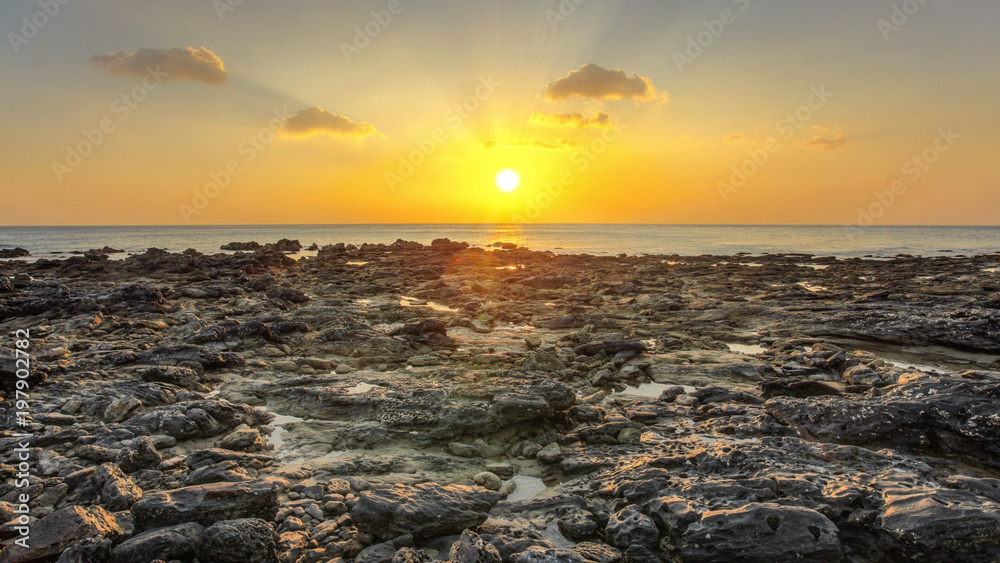 Rocky beach uncovered in low tide during evening sunset light with some clouds over horizon. Koh Lanta, Thailand
