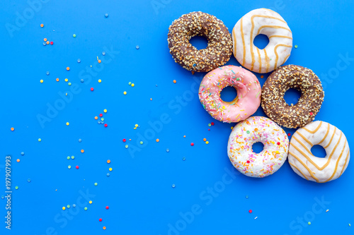 Donuts decorated icing and sprinkles on blue background top view copy space space for text