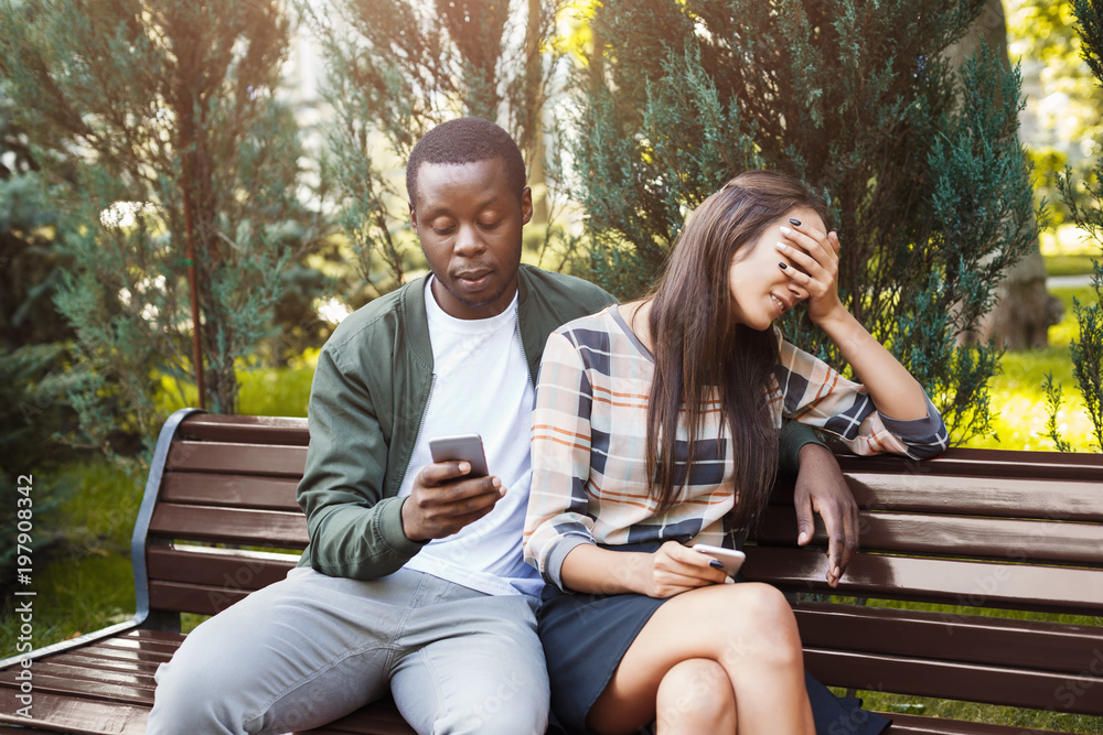 Fototapeta premium Woman sitting in park with man using smartphone