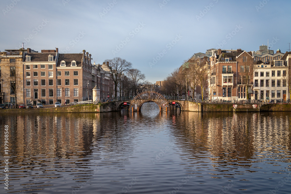water canals in Amsterdam with a bridge in the middle and buildings on both of bridge's side 