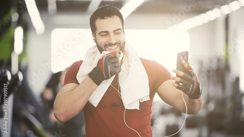 Athlete man wears red t-shirt with towel on neck talking via smartphone using headphones photo