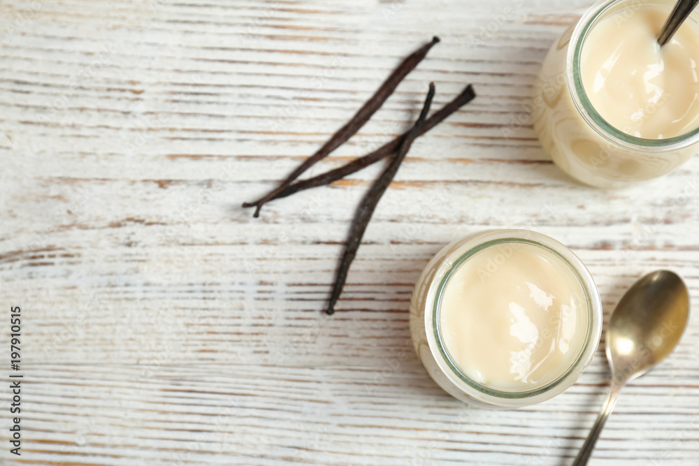 Jars with vanilla pudding and sticks on wooden background Jars with vanilla pudding and sticks on wooden background