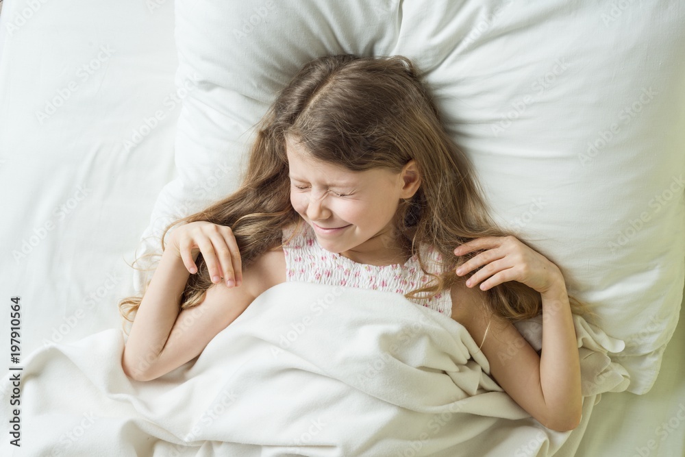 Good morning, Child girl blonde with long wavy hair wakes up, rubs eyes. Lying on a pillow in bed, top view. Good morning, Child girl blonde with long wavy hair wakes up, rubs eyes. Lying on a pillow in bed, top view.