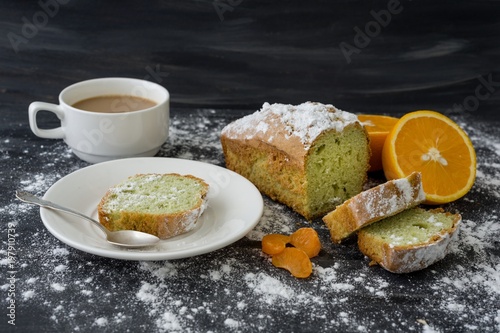 Mint cake sprinkled with powdered sugar on dark surface with fresh oranges mandarins