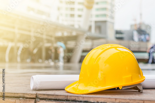 The yellow safety helmet and the blueprint at construction site with crane background