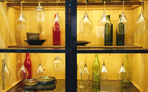 Colored dishes, bottles and hanging wine glasses on the shelves in the cupboard