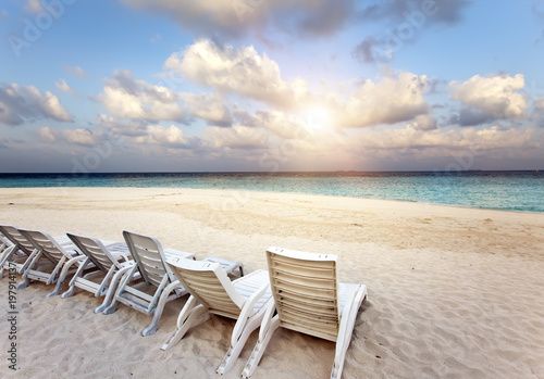 Beach lounge chairs on a beautiful tropical sand beach with cloudy blue sky. Maldives..