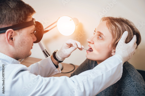 Otolaryngologist examines woman's throat with medical spatula. photo