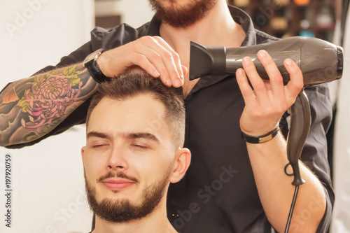 A young hairdresser who does a haircut and styling an attractive man in a hair salon