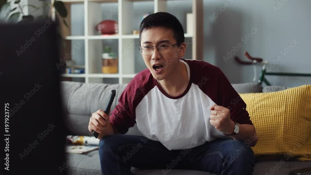 smiling attractive young chinese man with glasses sits on the couch and turns on the TV at home looking house technology male business bored leisure video sofa portrait close up slow motion smiling attractive young chinese man with glasses sits on the couch and turns on the TV at home looking house technology male business bored leisure video sofa portrait close up slow motion