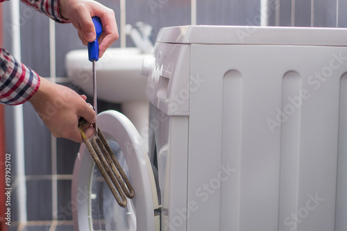 Washing machine repair. Repairer hands with screwdriver disassembling damaged unit of the heating element for repair photo