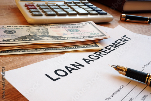 Loan agreement and dollar bills on an office desk.