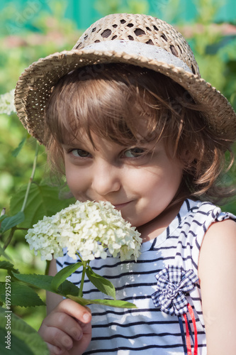 A little girl in a straw hat with a hydrangea branch, summertime vacation