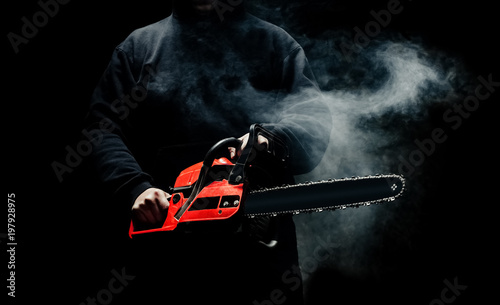 A man with a chainsaw in his hands close up against the background of smoke. photo